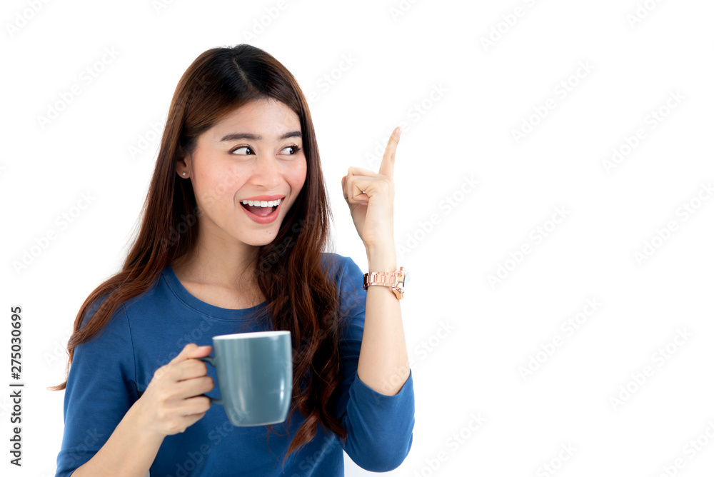 Happy Asian woman wearing blue sweater holding coffee mug and pointing up in white background. Happy Asian woman wearing blue sweater holding coffee mug and pointing up in white background.