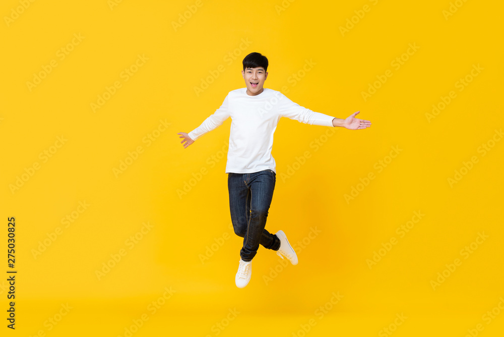 Excited asian man jumping over yellow background