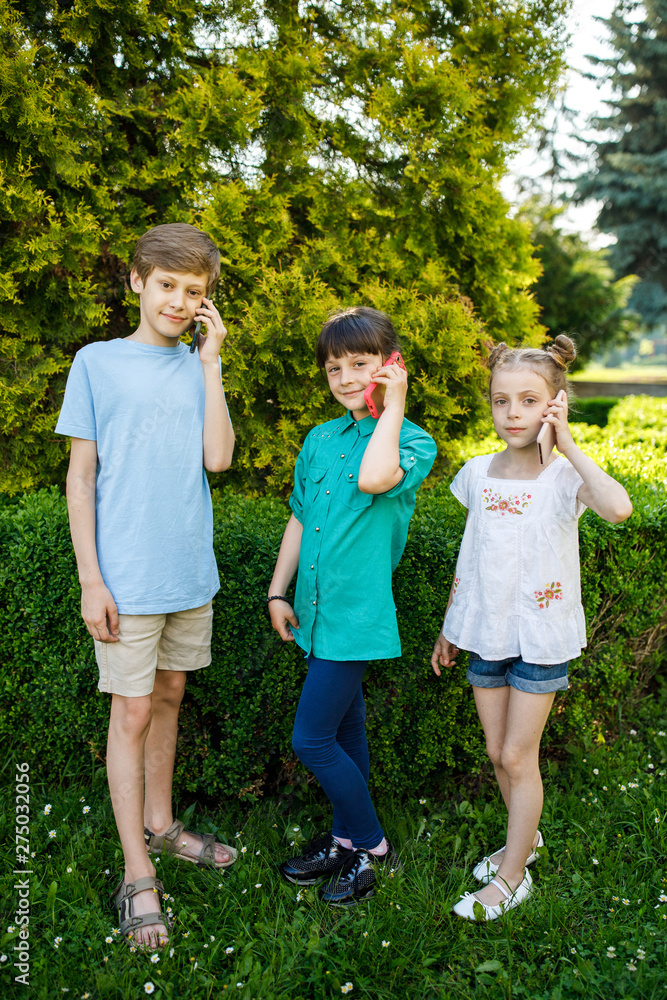 Cheerful children are talking on their smartphone on walking outside. Children are having fun Cheerful children are talking on their smartphone on walking outside. Children are having fun