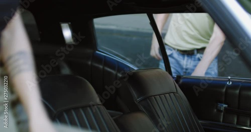 Beautiful Caucasian couple or friends sit inside an old classic retro muscle car, smiling and laughing. 4K UHD RAW graded footage