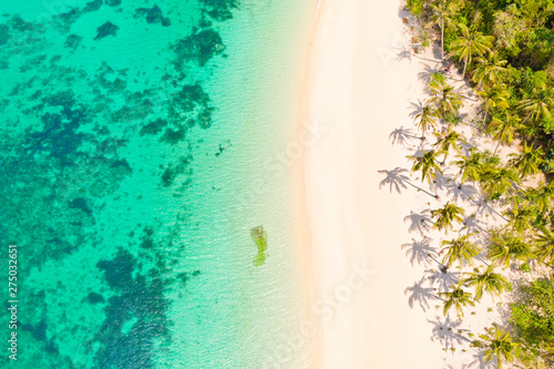 Turquoise lagoon with a coral reef and white beach. Beach with white sand and palm trees, view from above. Puka Shell Beach, Boracay Island, Philippines, aerial view.