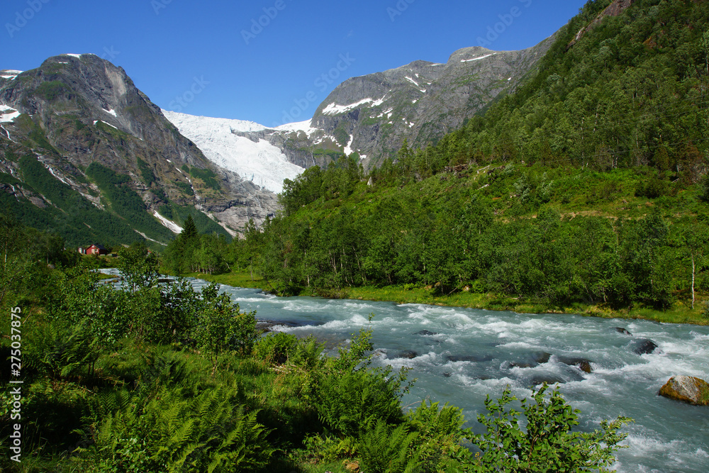 Travel to Norway, the blue mountain river flows among stones and bushes from a high mountain with a glacier