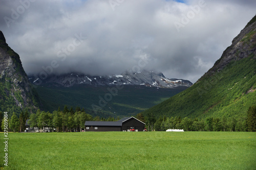 Travel to Norway, a green field in front of a mountain range, over which hung a dark cloud with rain