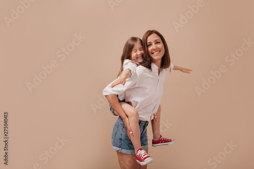 Obraz na płótnie Inspired young woman without make-up spending time with daughter, carrying her piggyback over isolated background. w salonie