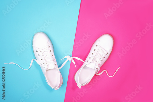 White sneakers are lying on bright neon color blue pink background. Top view. Flat lay. Copy space.