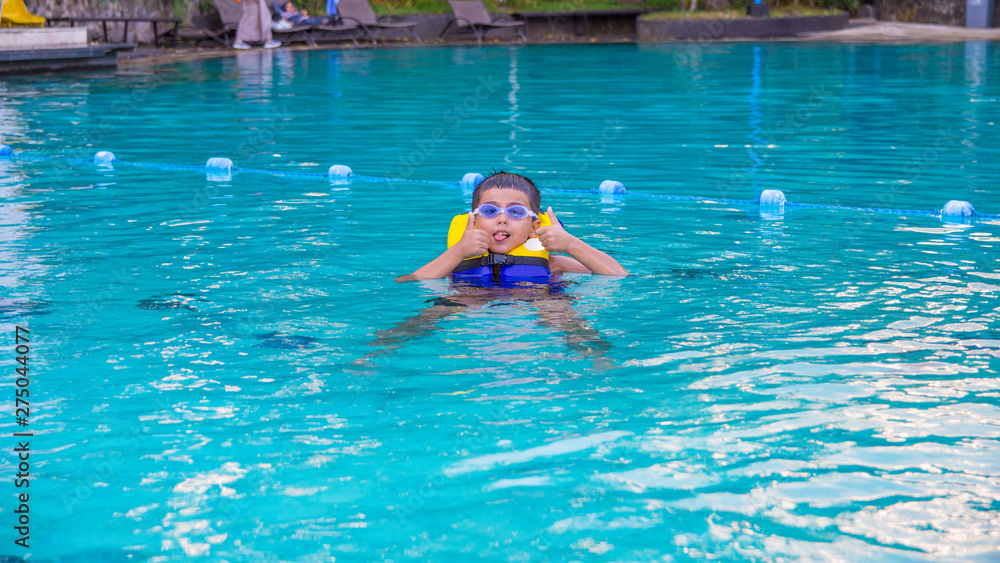 Boy swimming with life vest and googles on poking out his tongue looking very happy.