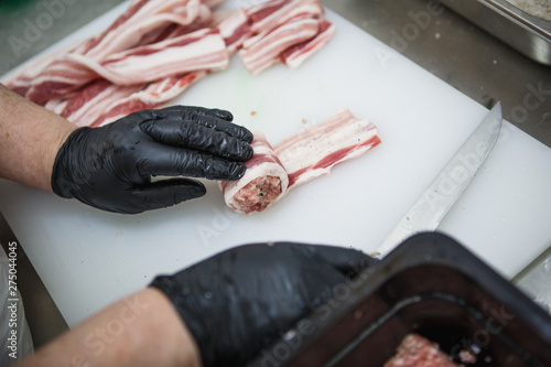 The process of preparing meat products. Gloved hands are molded from ground beef and bacon patties