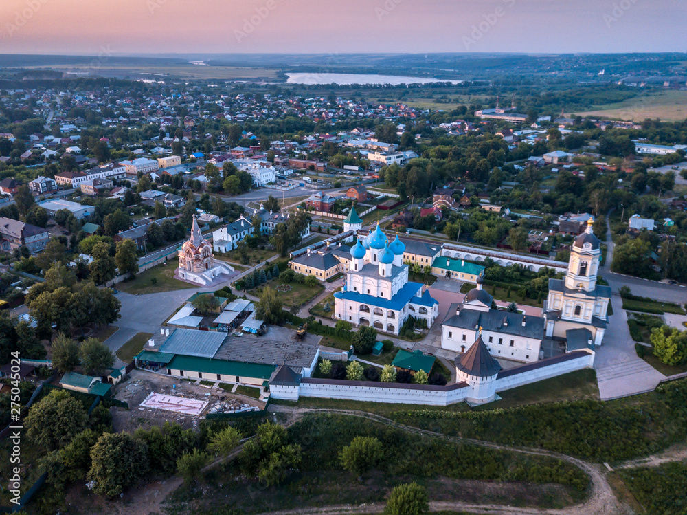 Fototapeta premium Aerial view of the ancient Orthodox Christian monastery, located among the houses and nature in the city of Serpukhov. Early summer morning. Moscow region