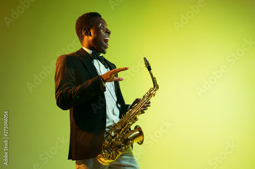 Canvas Print Young african-american jazz musician playing the saxophone on gradient yellow-green studio background