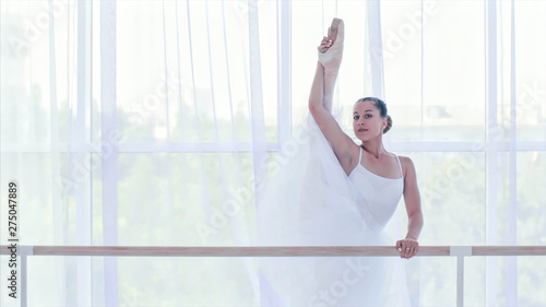 Obraz na płótnie Professional ballerina in white tutu is stretching near the barre stand