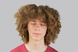portrait of a young curly European man with long curly hair and closed eyes close up dreaming. very lush male hair. curling hair for men. a lock of passion. isolated on gray background