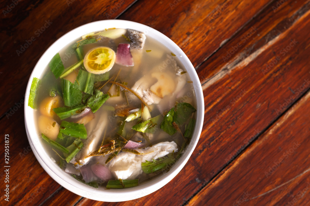 Spicy fish soup flavored with lemongrass and lime served on wooden table Spicy fish soup flavored with lemongrass and lime served on wooden table