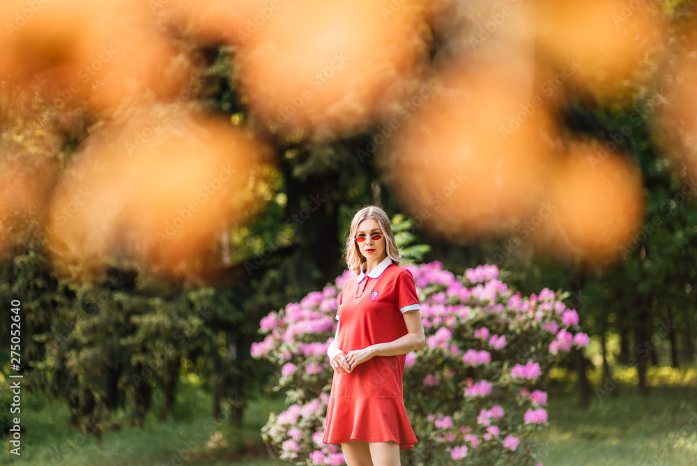 beautiful young girl in red dress and glasses walking in the park, woman is resting outdoors