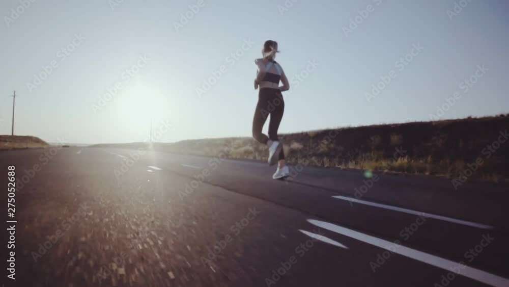 On the sunlit road with markings running sporty girl On the sunlit road with markings running sporty girl