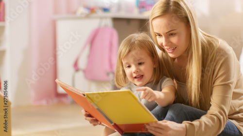 Beautiful Young Mother and Her Cute Little Daughter Read Children's Book Together. Children's Room is Pink and Full of Toys. photo