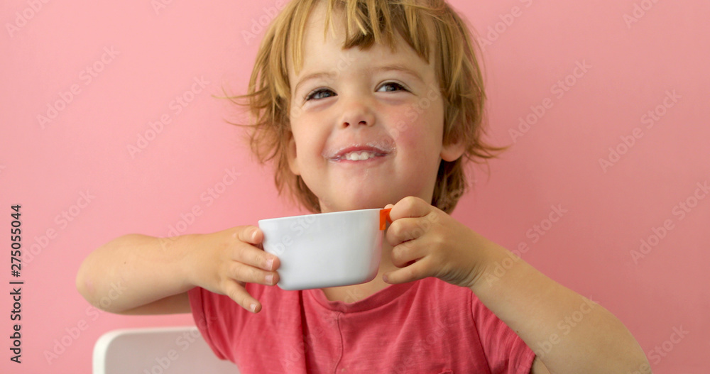 Happy child drinks milk from a cup on pink background Happy child drinks milk from a cup on pink background