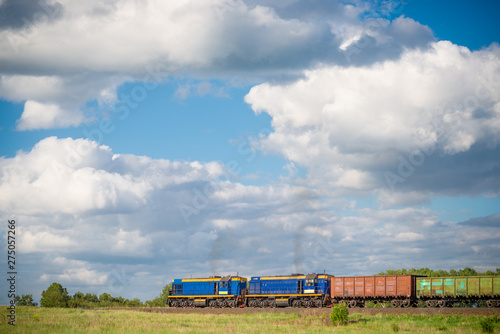 Rural summer landscape with freight train hauled by two diesel locomotives passing field at sunny day 