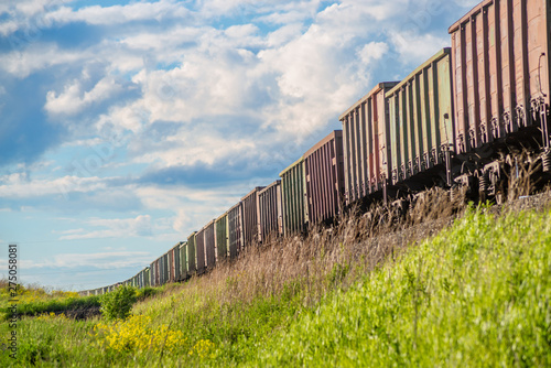 Rural summer landscape with freight train passing field at sunny day 