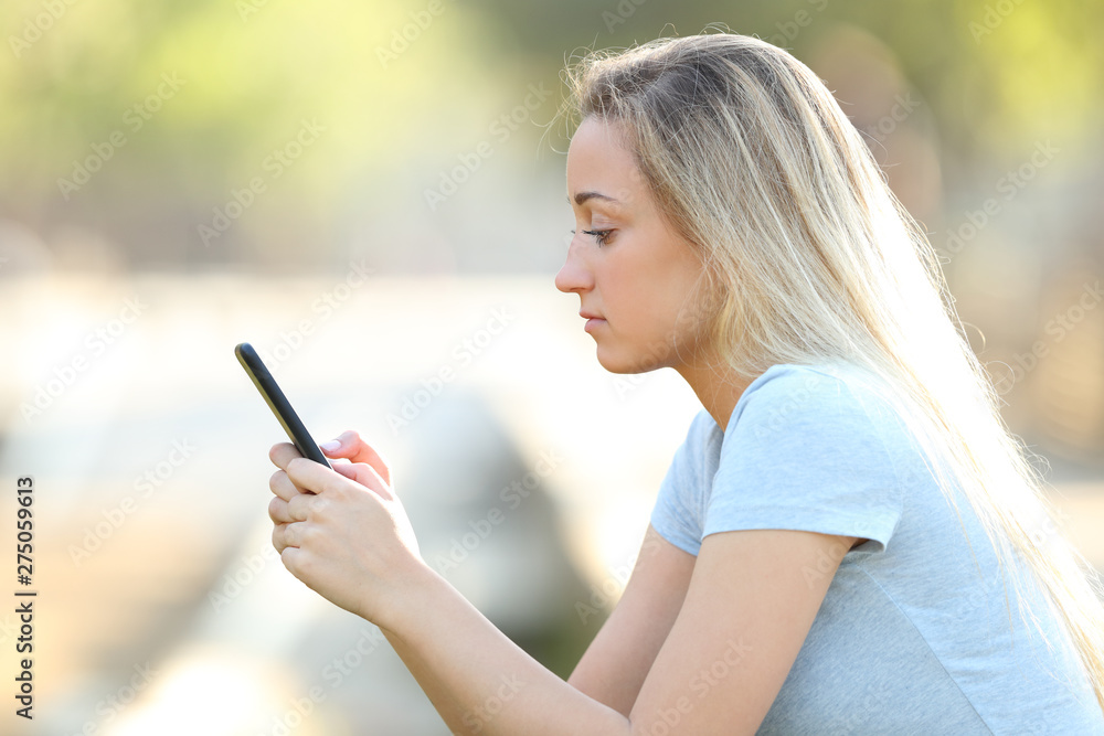 Profile of a teenage girl checking phone content in a park Profile of a teenage girl checking phone content in a park