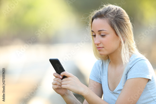 Serious teenage girl checking phone content in a park