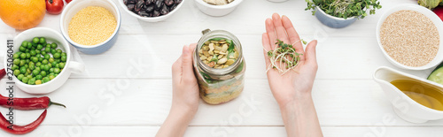 cropped view of woman adding sprouts in jar with salad on wooden white table, panoramic shot