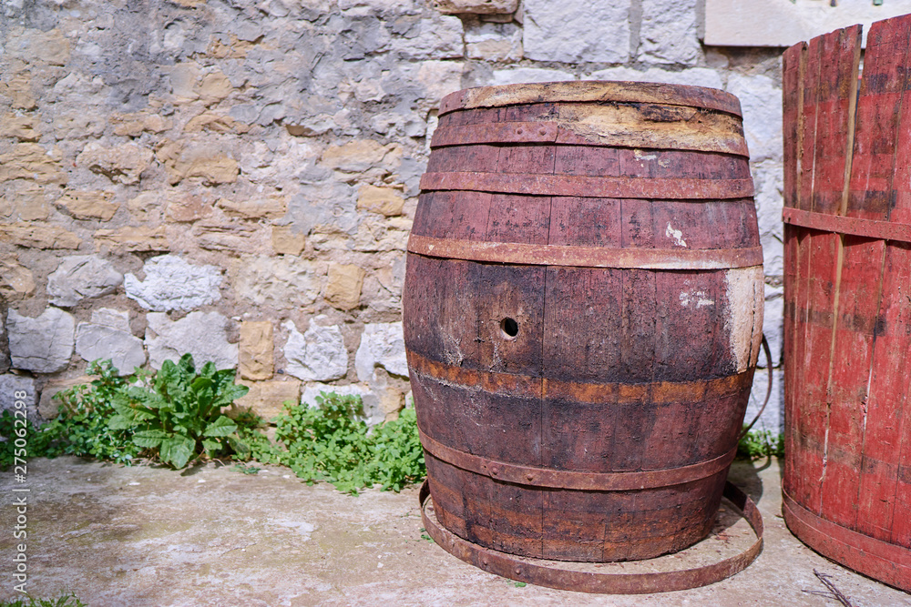 Old wooden keg or barrel against stone wall outdoors.