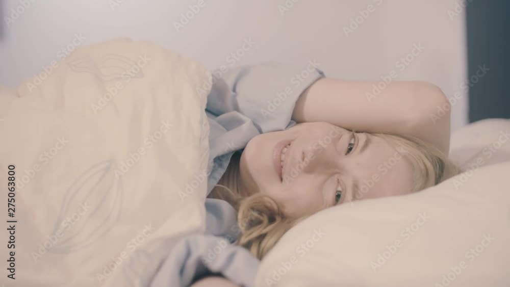 Young woman in bed waking up smiling and stretching, looking at the camera - slow motion Young woman in bed waking up smiling and stretching, looking at the camera - slow motion