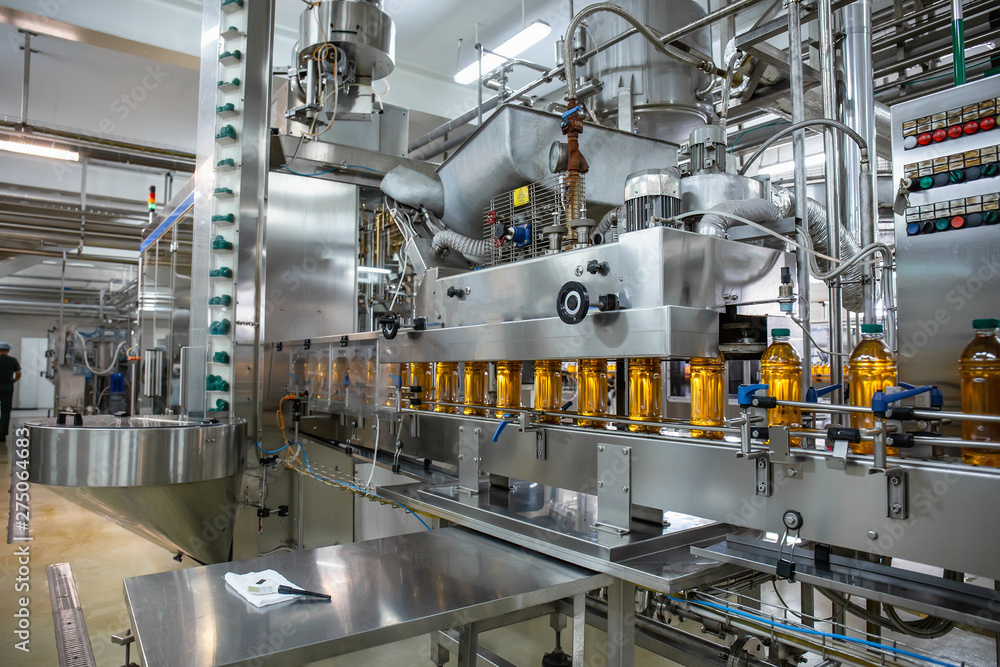 Conveyor belt or line in beverage plant with modern industrial machine equipment. Plastic bottles with fresh organic juice in factory interior Conveyor belt or line in beverage plant with modern industrial machine equipment. Plastic bottles with fresh organic juice in factory interior
