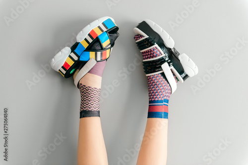 Beautiful female legs in mismatched trendy socks posing in two different fashionable high wedge leather sandals on gray background. Odd disargonized  young girl wearing high sole summer stylish shoes.