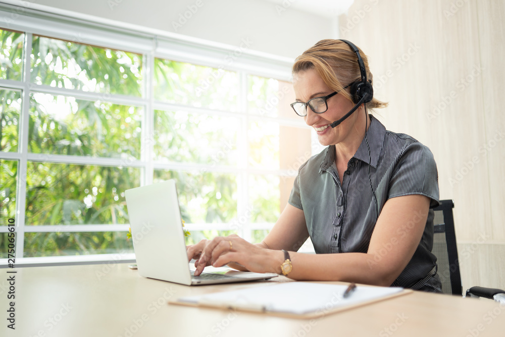 Smiling woman in working on laptop and headset in call center. Smiling woman in working on laptop and headset in call center.