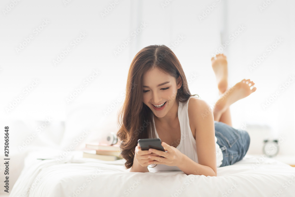 female while using cell phone while lying on her bed. female while using cell phone while lying on her bed.