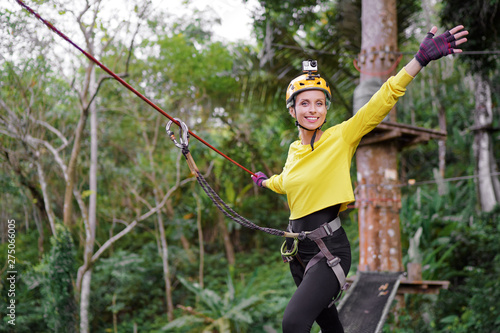 Young woman with climbing gear in an adventure extreme park climbing or passing on the rope road.