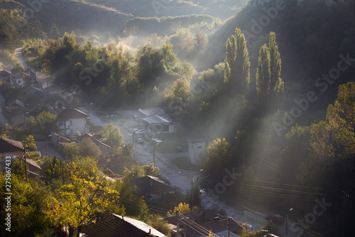 Aerial view of beautiful foggy village between mountains in Lovech, Bulgaria. Misty sunrise view of city district surrounded by rock mountain. Sun beams between trees