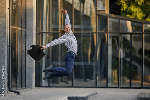 Crazy young businessman dancing on the street with bag. Celebrating victory. Flexibility and grace in business