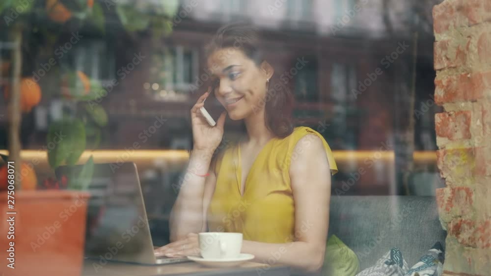 Attractive student brunette is talking on mobile phone working with laptop in modern cafe enjoying leisure time alone. People, technology and communication concept. Attractive student brunette is talking on mobile phone working with laptop in modern cafe enjoying leisure time alone. People, technology and communication concept.
