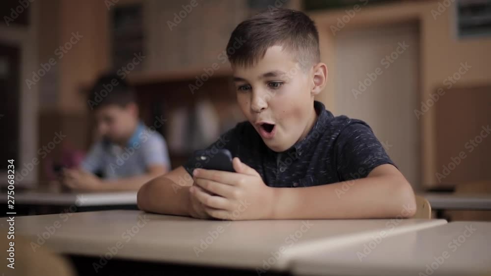 Cute little boy use phone during lesson. Two schollboy in class Cute little boy use phone during lesson. Two schollboy in class