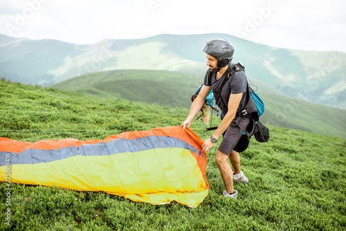 Well-equipped man preparing for the flight, laying out the paraglider on the green meadow high in the mountains