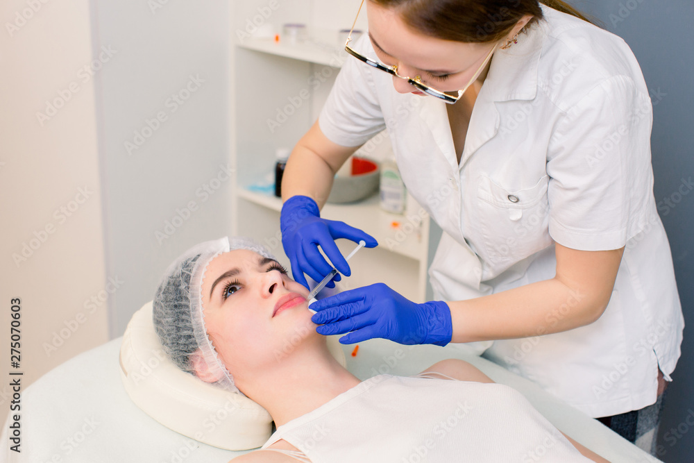 The doctor cosmetologist makes Lip augmentation procedure of a beautiful woman in a beauty salon. Cosmetology skin care. The doctor cosmetologist makes Lip augmentation procedure of a beautiful woman in a beauty salon. Cosmetology skin care.