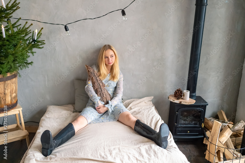 Stylish girl in rubber boots siiting on bed and posing with decorative log  in her hands in rural room with christmas tree. Odd people concept. Stock  Photo | Adobe Stock
