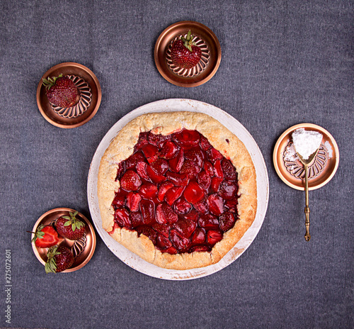 Summer strawberry pie cake galette and cooper saucer with strawberries over on gray background. Top view photo