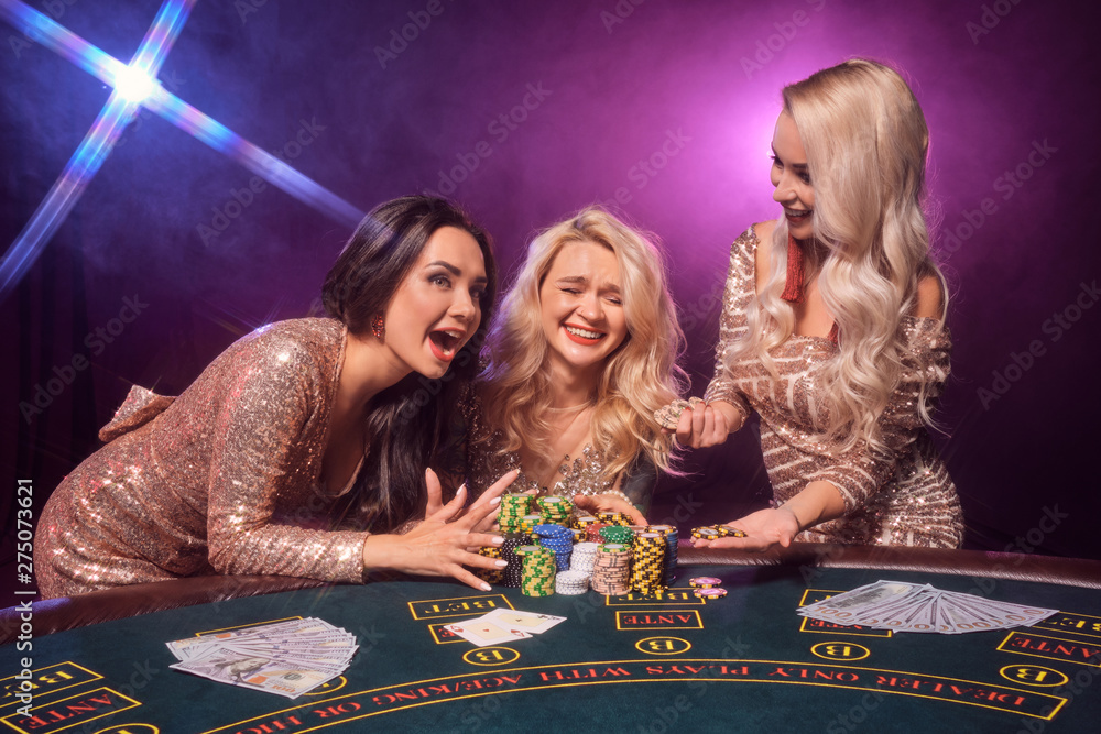 Beautiful girls with a perfect hairstyles and bright make-up are posing standing at a gambling table. Casino, poker. Beautiful girls with a perfect hairstyles and bright make-up are posing standing at a gambling table. Casino, poker.