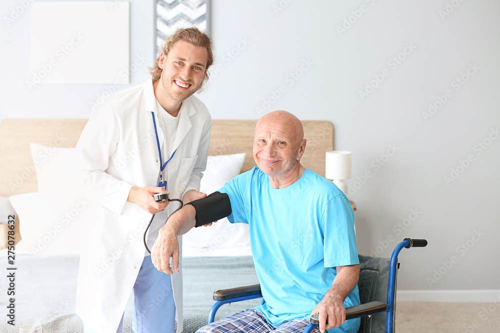 Fototapeta premium Doctor measuring pressure of elderly man in nursing home