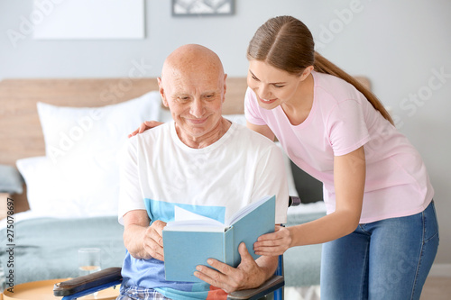 Young woman reading book with her father in nursing home