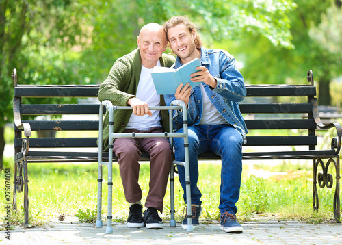 Young man reading book to his elderly father in park