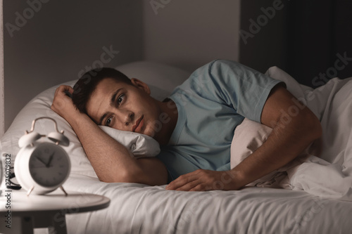 Young man suffering from insomnia while lying in bed at night photo
