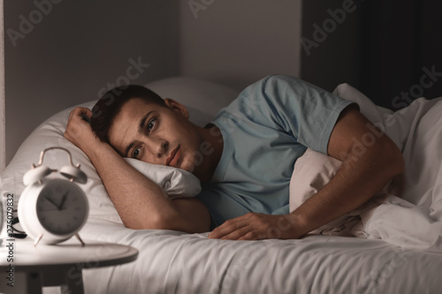 Young man suffering from insomnia while lying in bed at night