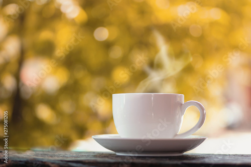 hot coffee cup on wooden table over nature autumn background with morning sunlight