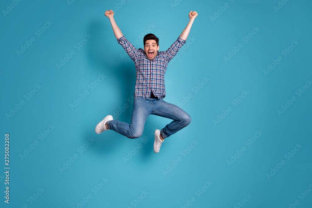 Full length body size view photo charming nice youngster raise fists shout yeah celebrate wonderful news thrilled candid checked shirt jeans sneakers free time holiday isolated blue background