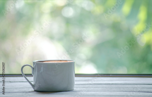 Hot coffee cup with white the wooden table and the Green leaf background with copy space on right