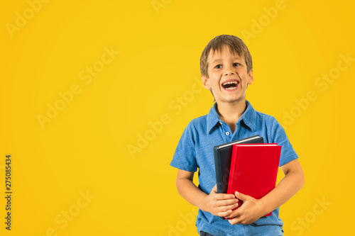 Happy pupil schoolboy with books on yellow background.